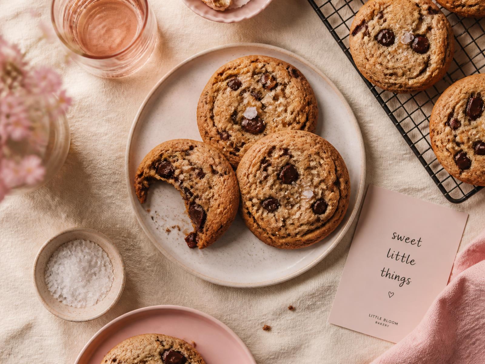 Freshly baked chocolate chunk cookies with sea salt on a cream linen table
